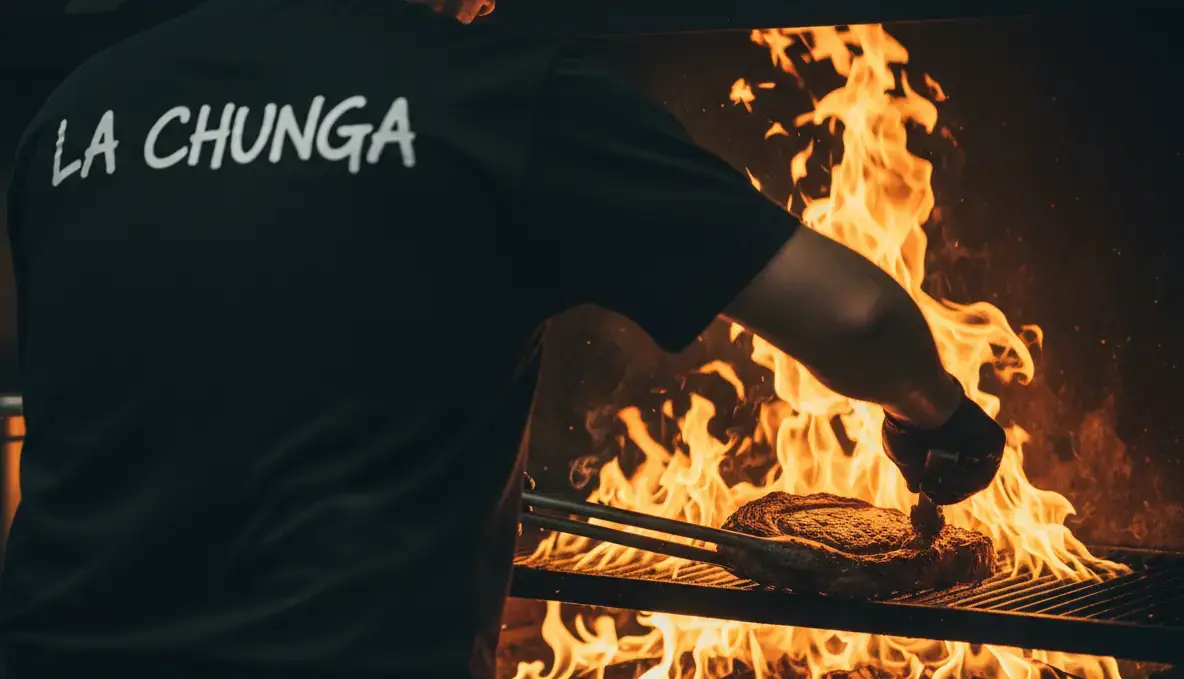 Un cuisinier de La Chunga, de dos, devant un grill en flammes