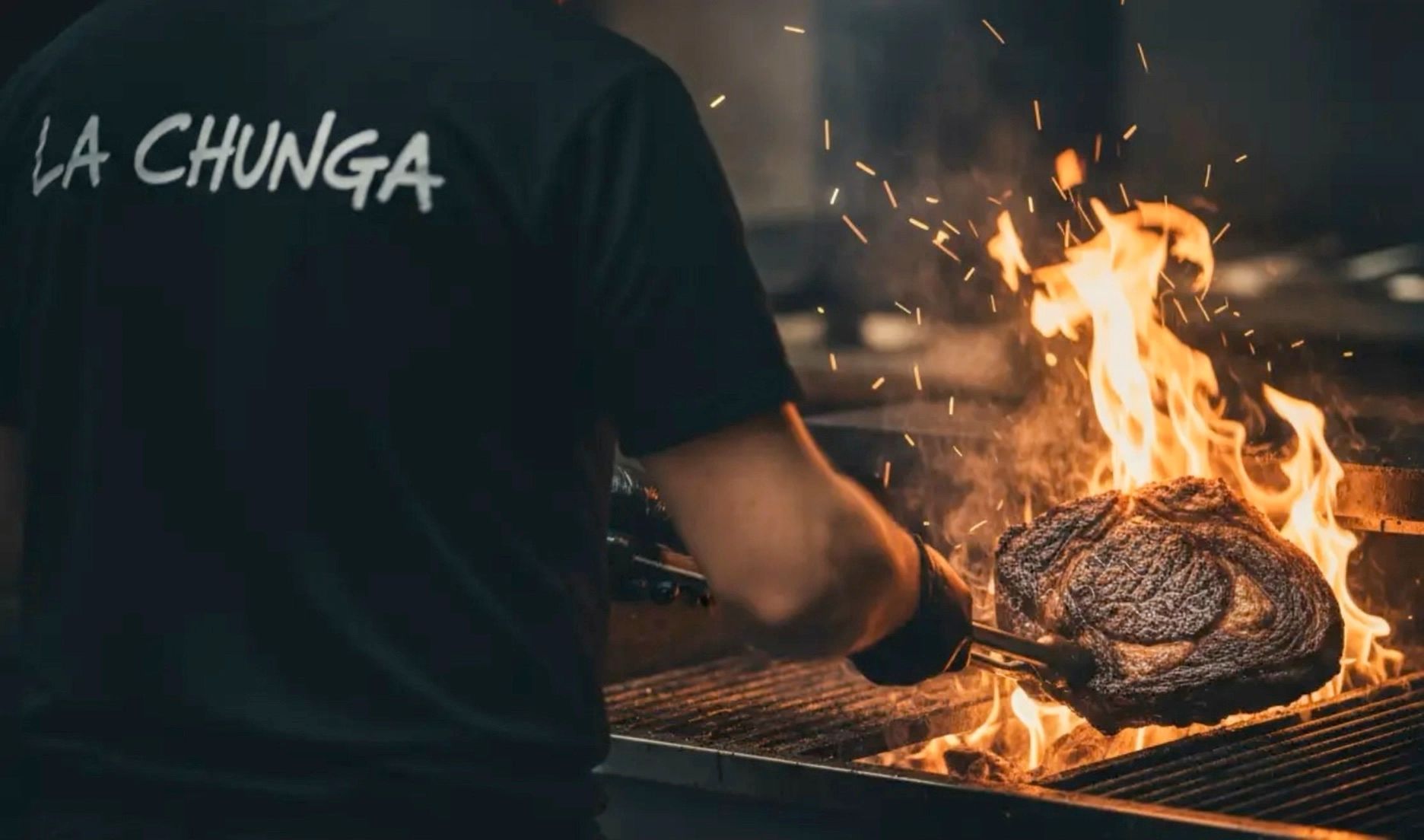 Un cuisinier de La Chunga saisit une côte de bœuf au-dessus des flammes
